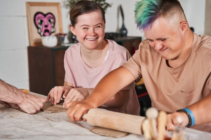 Zwei Mädchen mit besonderen Bedürfnissen rollen lachend Teig aus