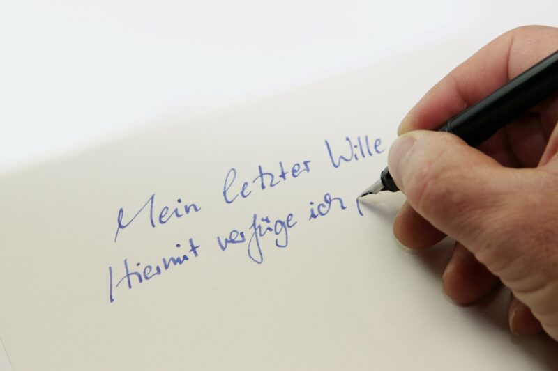 Eine Hand scheibt auf ein Papier: Mein letzter Wille. Hiermit verfüge ich ...